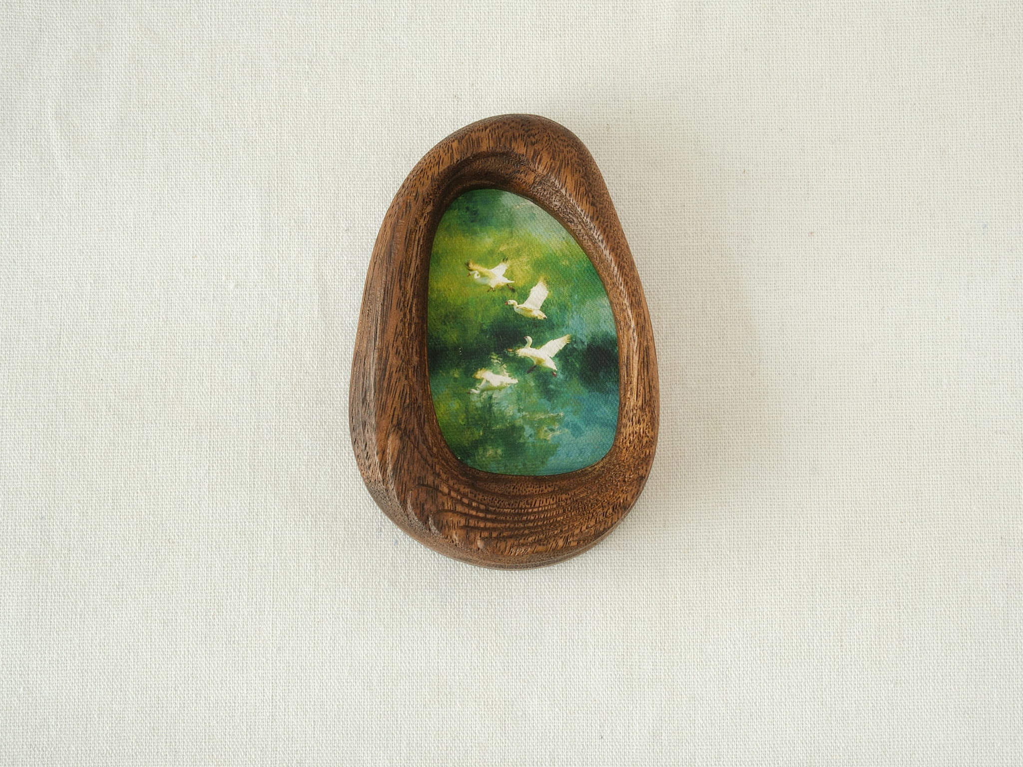 Front view of the Waterdrop handmade solid wood art frame featuring birds flying over a lush forest, highlighting the organic pebble shape and natural wood grain.