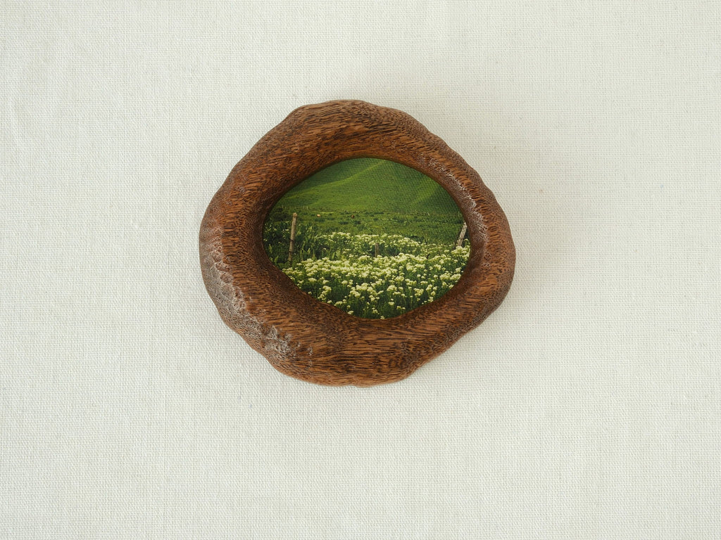 Front view of the lake-shaped organic solid wood frame, featuring a serene landscape painting of a green meadow filled with white wildflowers.