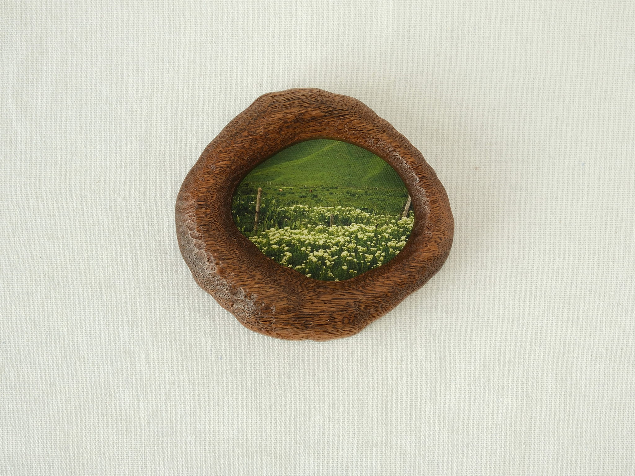 Front view of the lake-shaped organic solid wood frame, featuring a serene landscape painting of a green meadow filled with white wildflowers.