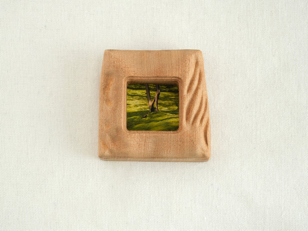 Front view of a handmade square mini picture frame with "Moderno Organico" wavy hand-carved edges, showcasing the rich reddish-brown texture of solid wood and a serene mossy forest painting.