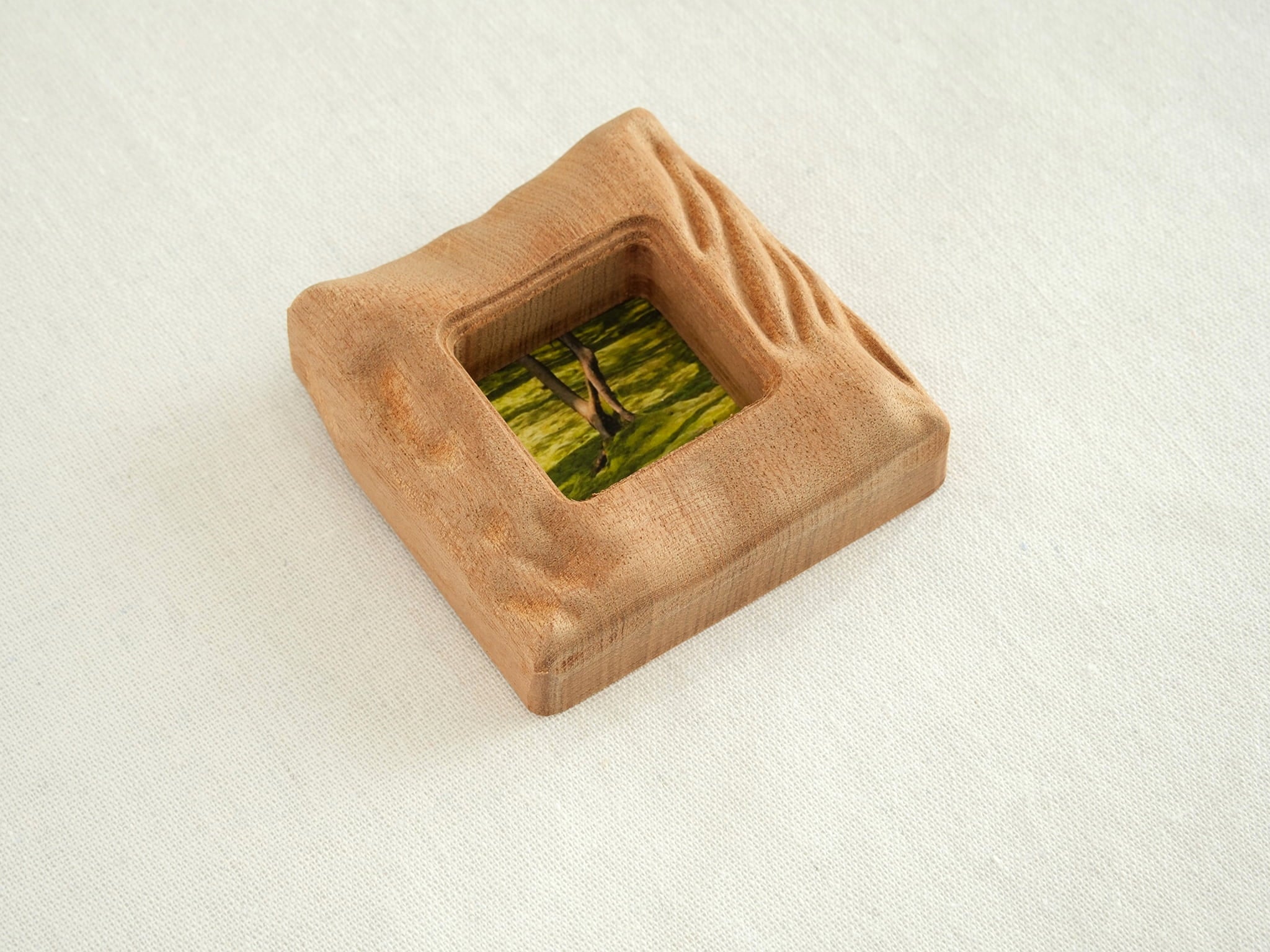An isometric, high-angle view of the handmade solid wood mini frame, showcasing the substantial thickness and the intricate, hand-carved wavy texture along the right side. The natural reddish-brown grain of Sapele wood is prominent on the curved edges.