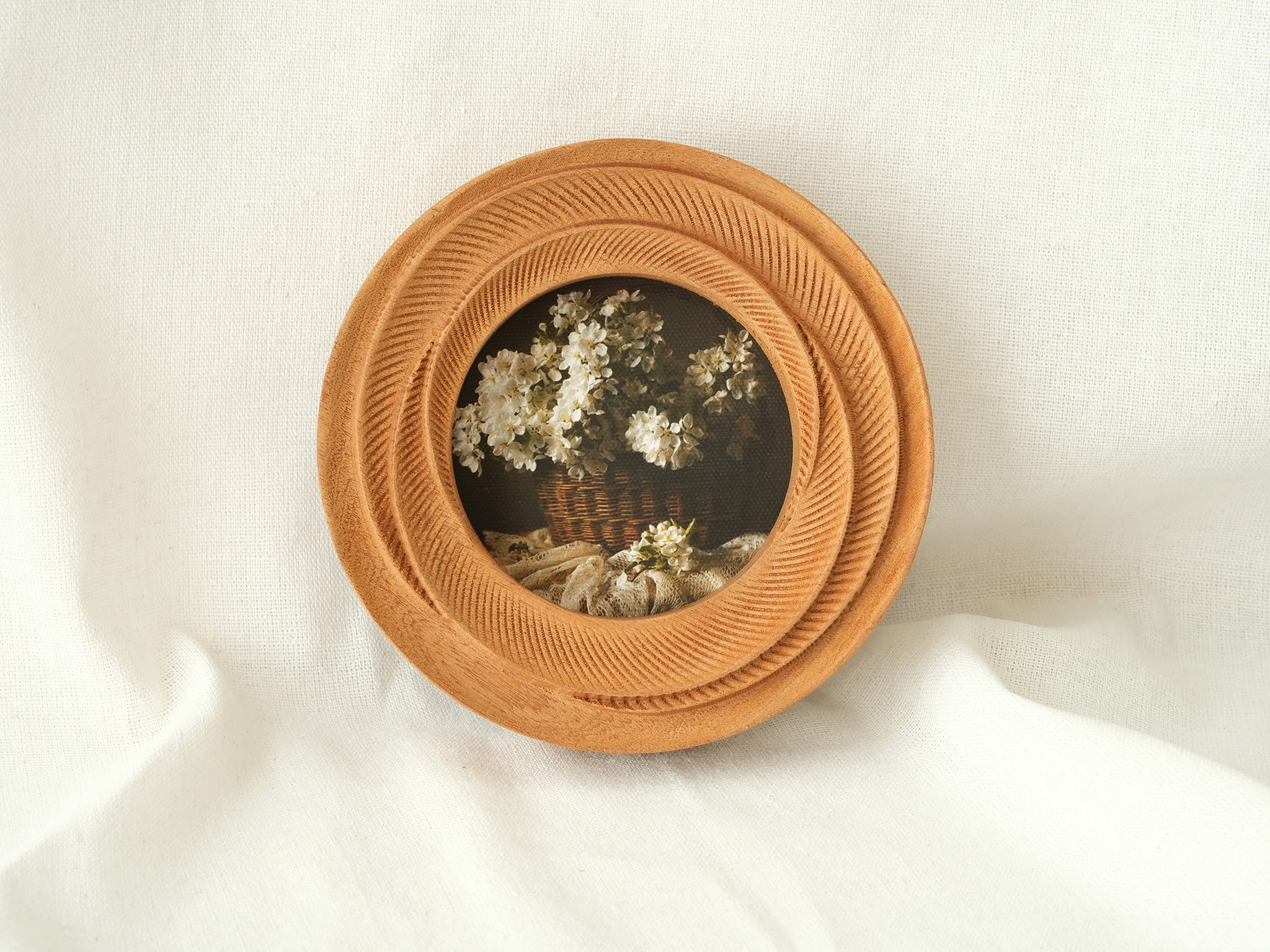 The round flower frame leaning against white fabric, showcasing its radiant tiered textures as artistic desktop decor.
