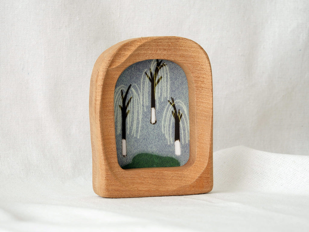 A soft arched wood frame standing firmly on a white textured surface, showcasing its gentle organic silhouette.