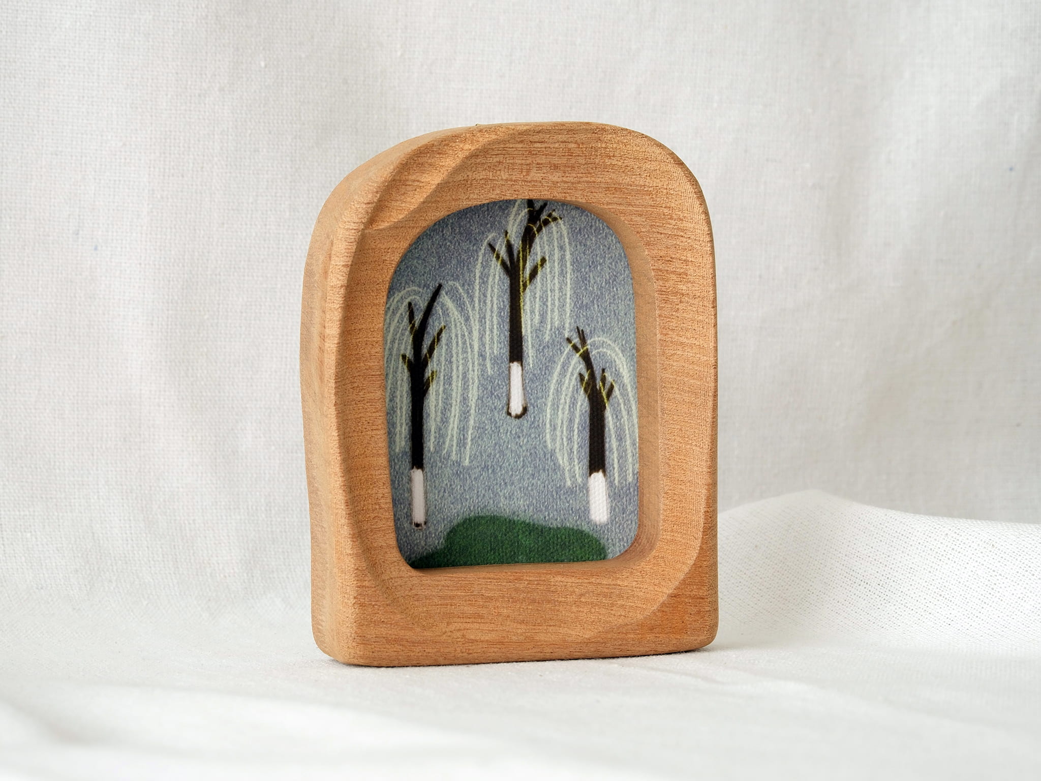 A soft arched wood frame standing firmly on a white textured surface, showcasing its gentle organic silhouette.