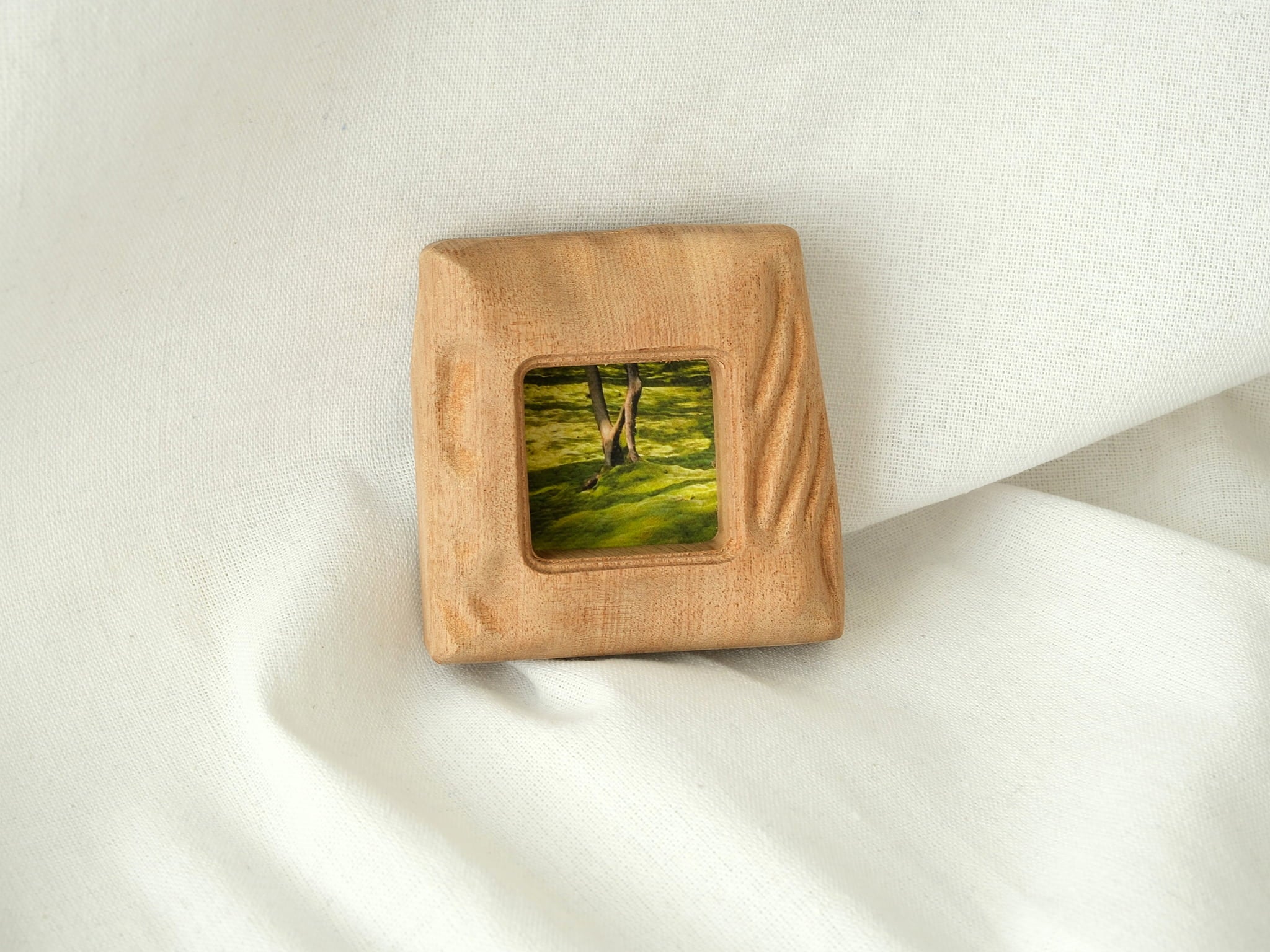 A direct front view of the mini solid wood frame leaning gently against a plain white wall. The natural daylight accentuates the deeply sculpted, fluid "Moderno Organico" wavy patterns on the frame's right side, casting subtle shadows.