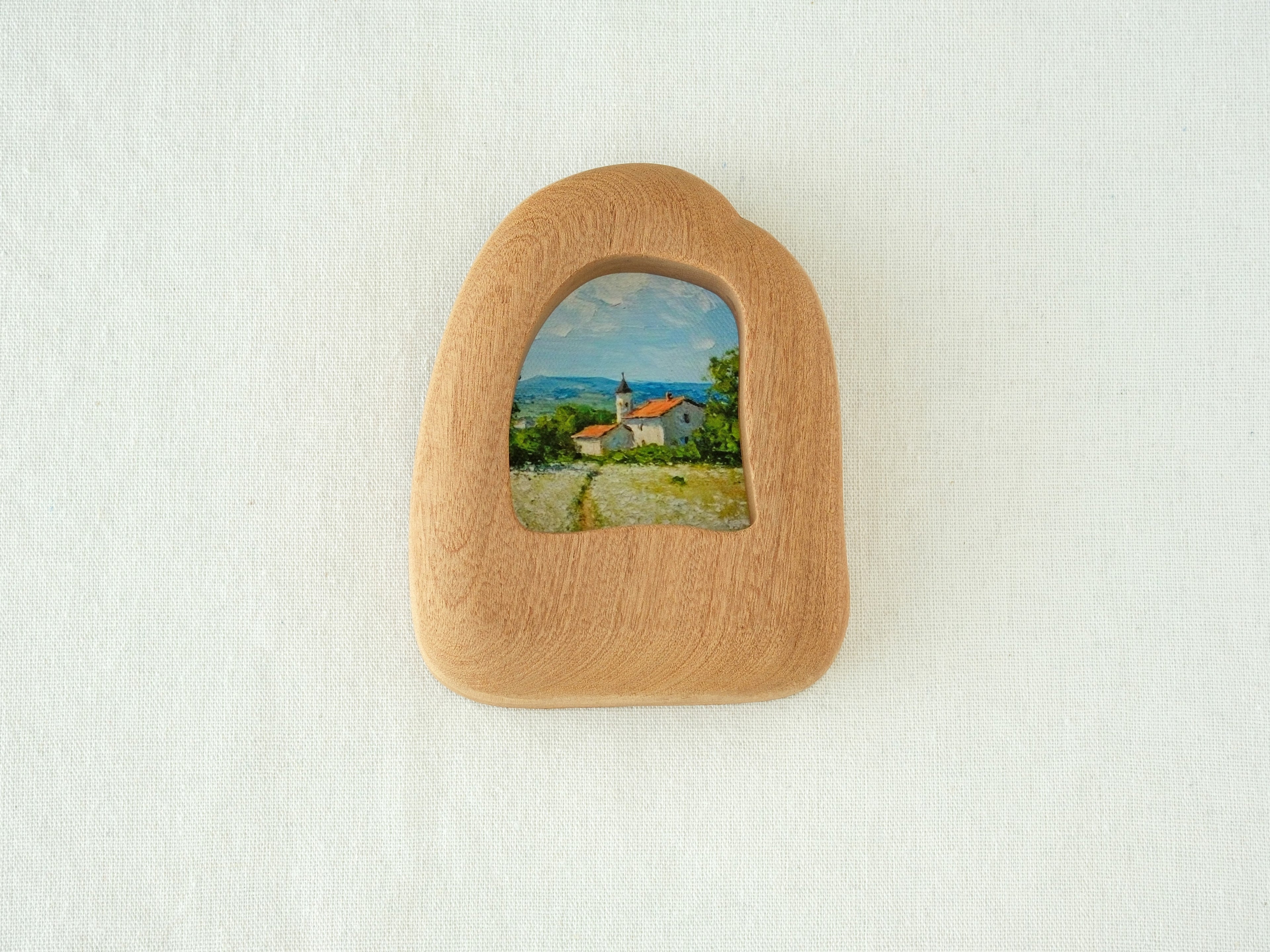 House-shaped wood frame leaning against a soft white textured wall, creating a cozy and natural aesthetic.