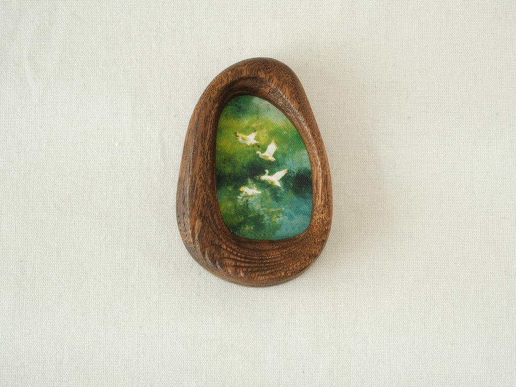 Front view of the Waterdrop handmade solid wood art frame featuring birds flying over a lush forest, highlighting the organic pebble shape and natural wood grain.