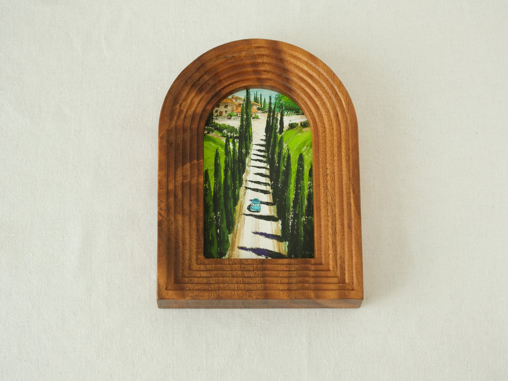 Front view of the arched solid wood frame "Tuscany," featuring a handcrafted stepped border and an oil-style painting of a cypress-lined road leading to an Italian villa.