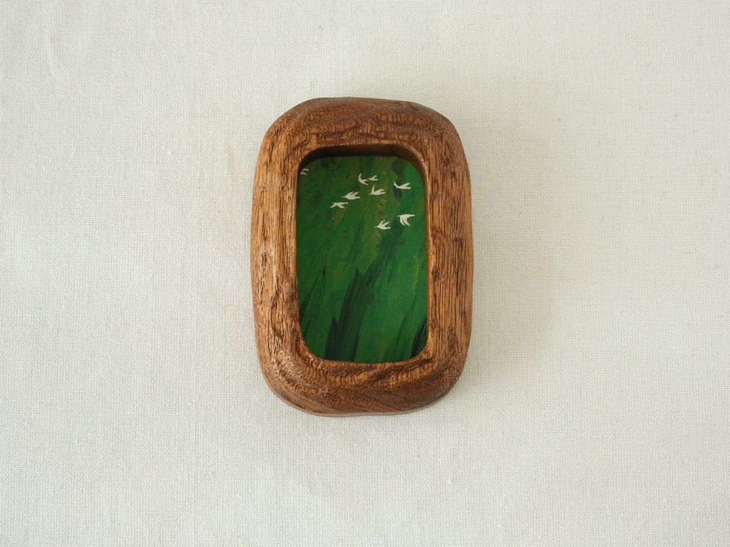 Front view of the Rounded Rectangle handmade solid wood art frame in a vertical orientation, featuring a painting of white birds flying over a dense green forest.