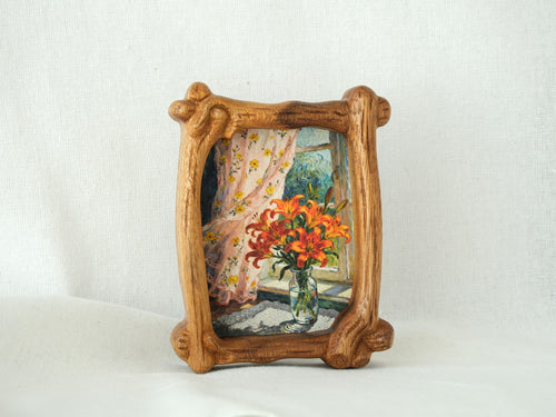 Handcrafted organic shaped solid wood picture frame with a natural grain finish, displayed on a white fabric background as a tabletop decorative art piece.