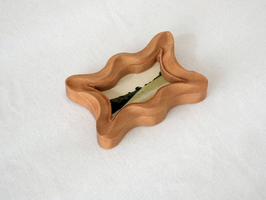 Angled top view of the rippled wave wood frame, highlighting its deep fluid ridges and intricate hand-sculpted texture.