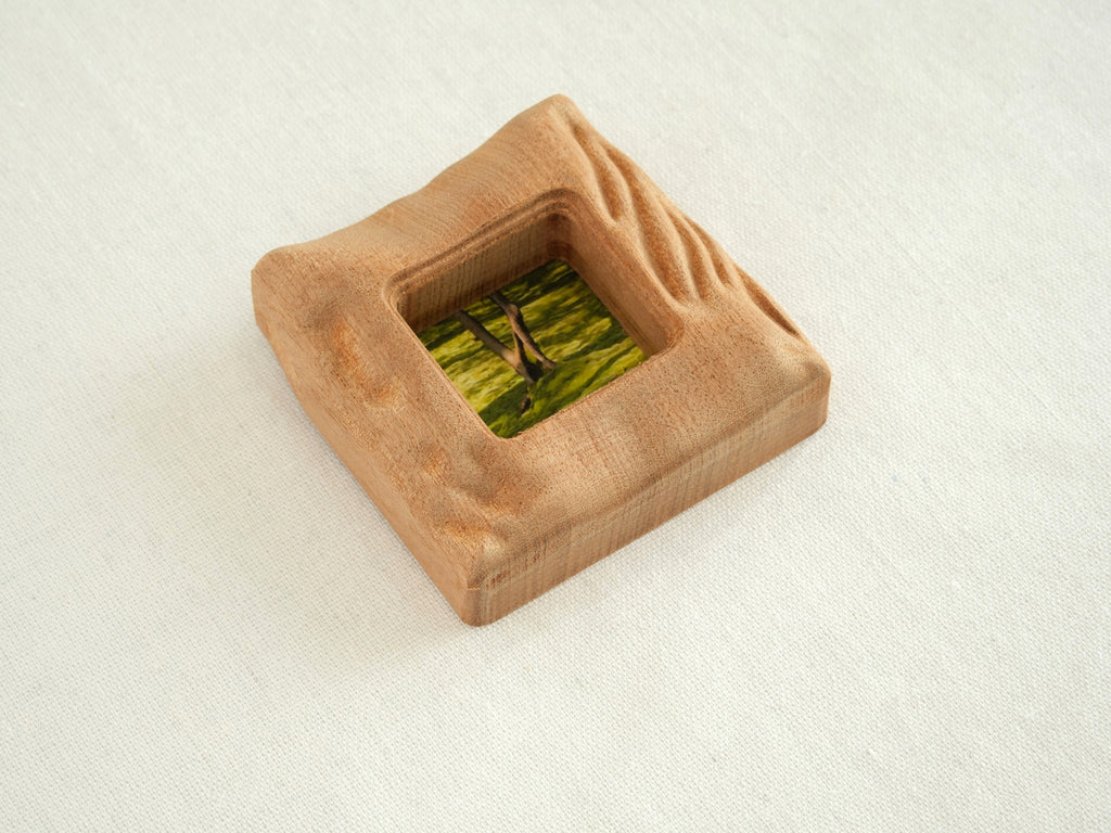 An isometric, high-angle view of the handmade solid wood mini frame, showcasing the substantial thickness and the intricate, hand-carved wavy texture along the right side. The natural reddish-brown grain of Sapele wood is prominent on the curved edges.