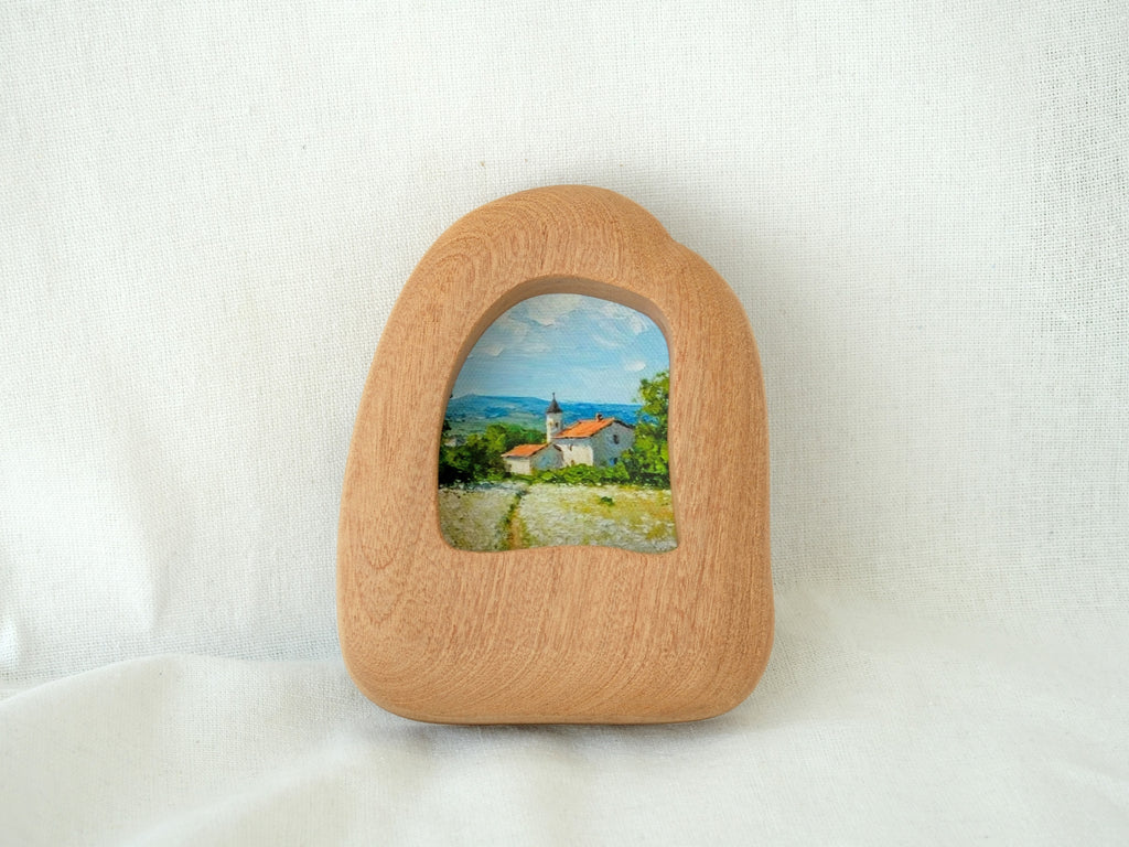 Front view of a house-shaped wood frame, featuring a hand-carved organic silhouette and warm Sapele grain.