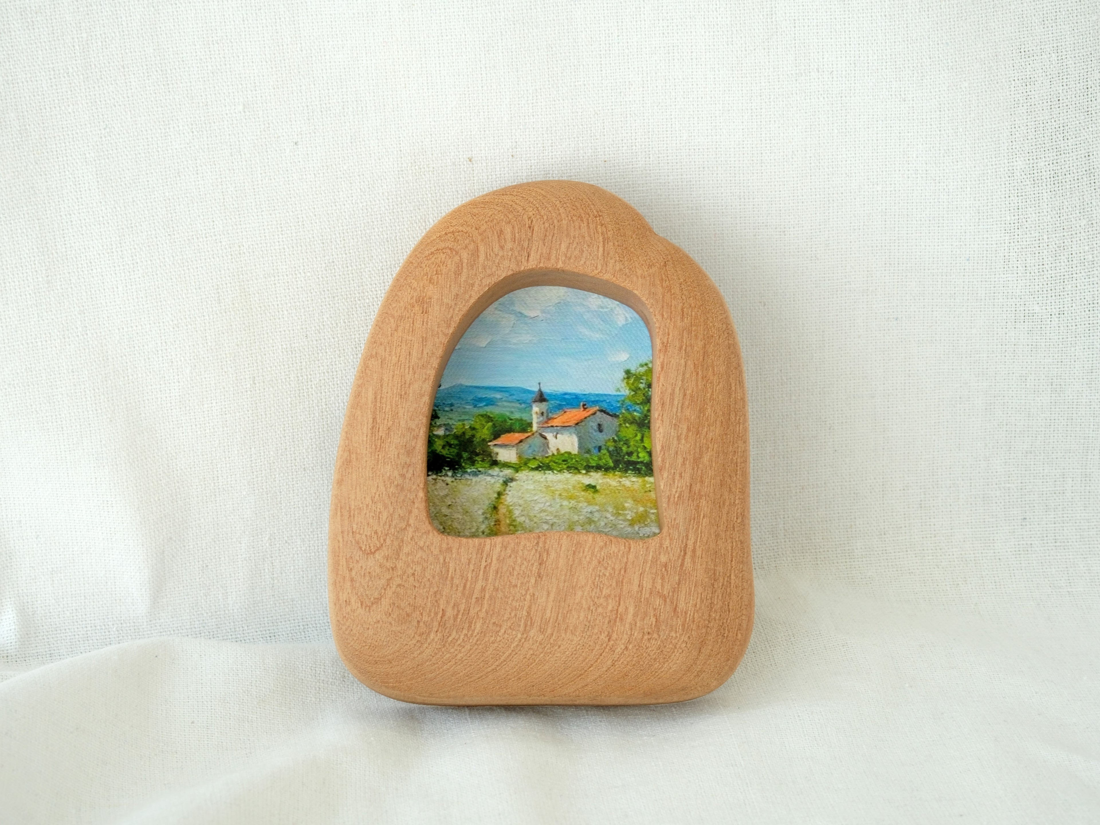 Front view of a house-shaped wood frame, featuring a hand-carved organic silhouette and warm Sapele grain.