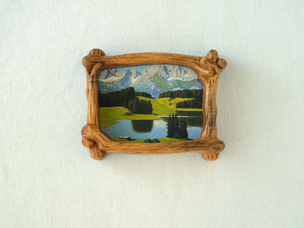 A direct front view of a nature-inspired wood frame with intricate hand-carved bark details, showcasing a lush green forest art piece.