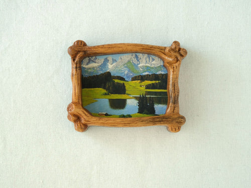 A direct front view of a nature-inspired wood frame with intricate hand-carved bark details, showcasing a lush green forest art piece.