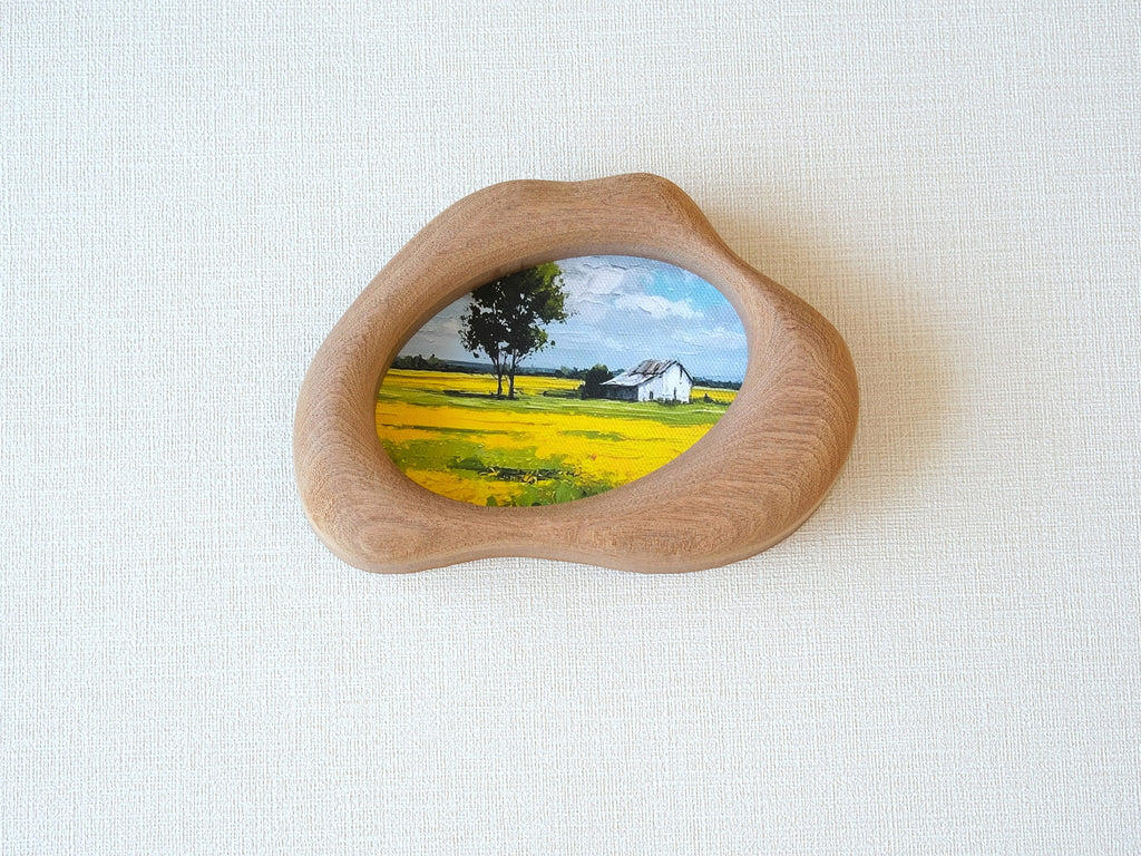 A front view of the handmade solid wood art frame featuring a soft, organic cloud-shaped silhouette. The smooth, hand-sculpted curves of the wood encase a landscape painting, creating the aesthetic of a floating piece of nature.