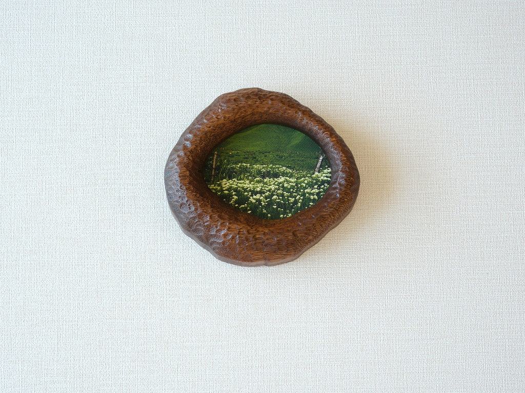 Front view of the lake-shaped organic solid wood frame, featuring a serene landscape painting of a green meadow filled with white wildflowers.