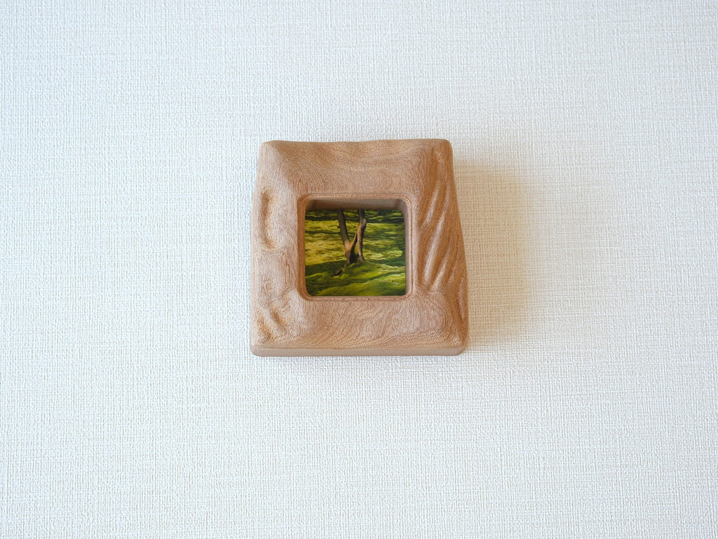 Front view of a handmade square mini picture frame with "Moderno Organico" wavy hand-carved edges, showcasing the rich reddish-brown texture of solid wood and a serene mossy forest painting.