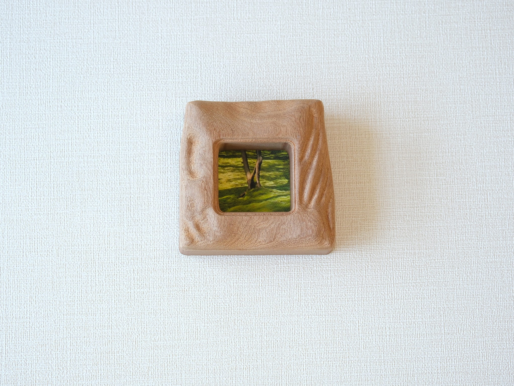Front view of a handmade square mini picture frame with "Moderno Organico" wavy hand-carved edges, showcasing the rich reddish-brown texture of solid wood and a serene mossy forest painting.