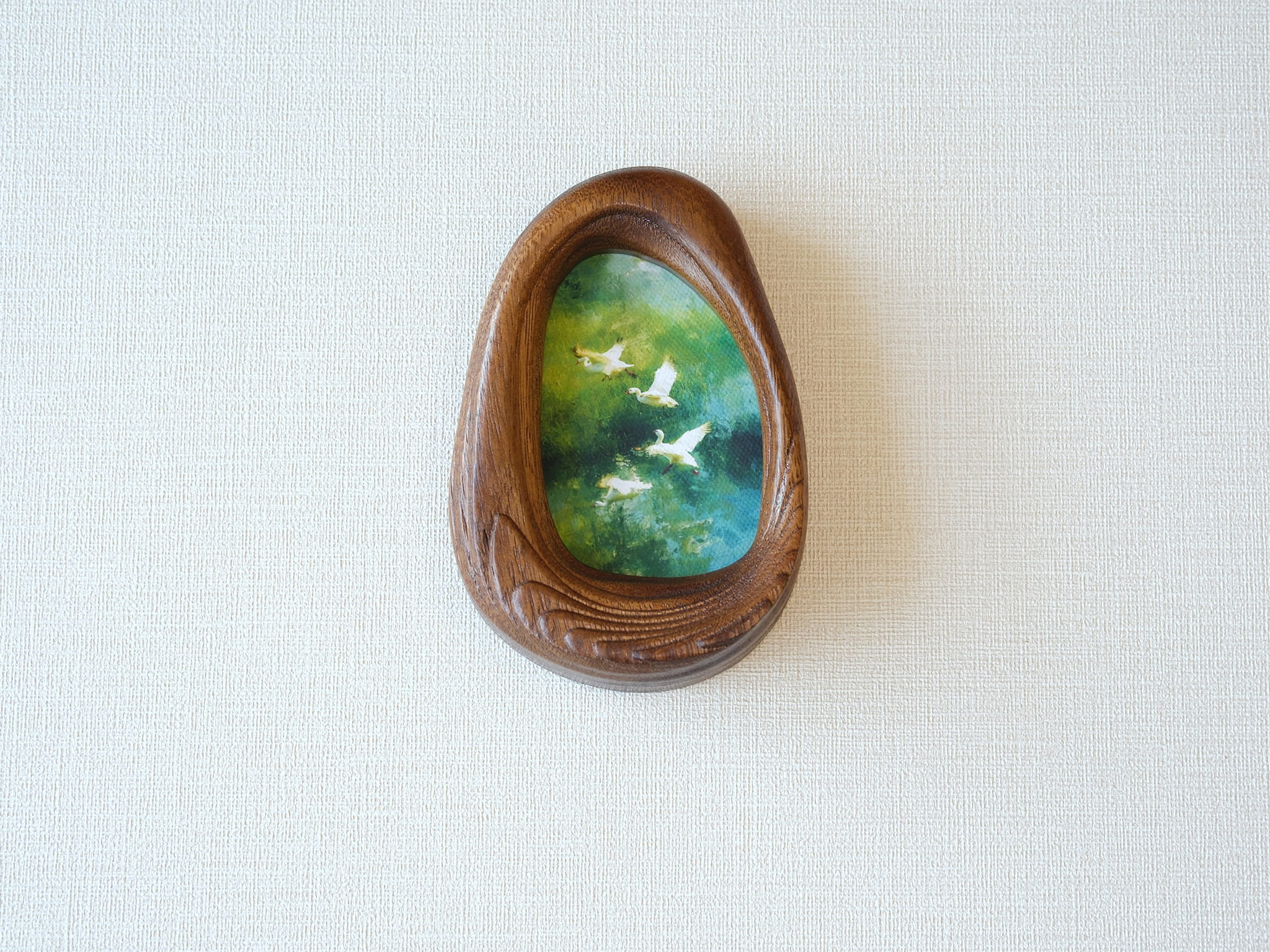 Front view of the Waterdrop handmade solid wood art frame featuring birds flying over a lush forest, highlighting the organic pebble shape and natural wood grain.