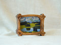 A side-angle view of a handcrafted wood frame with an organic branch-like texture, featuring a vibrant forest sunlight oil painting.