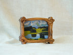 A side-angle view of a handcrafted wood frame with an organic branch-like texture, featuring a vibrant forest sunlight oil painting.