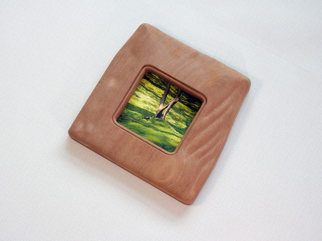 Large handmade solid wood picture frame with green forest artwork, high-angle side view.