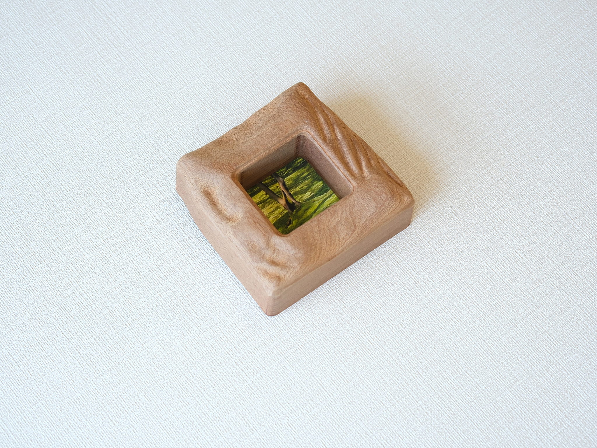 An isometric, high-angle view of the handmade solid wood mini frame, showcasing the substantial thickness and the intricate, hand-carved wavy texture along the right side. The natural reddish-brown grain of Sapele wood is prominent on the curved edges.