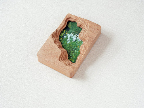 Handmade solid wood wall art frame with organic lake-shaped cutout and floral meadow artwork, side view.