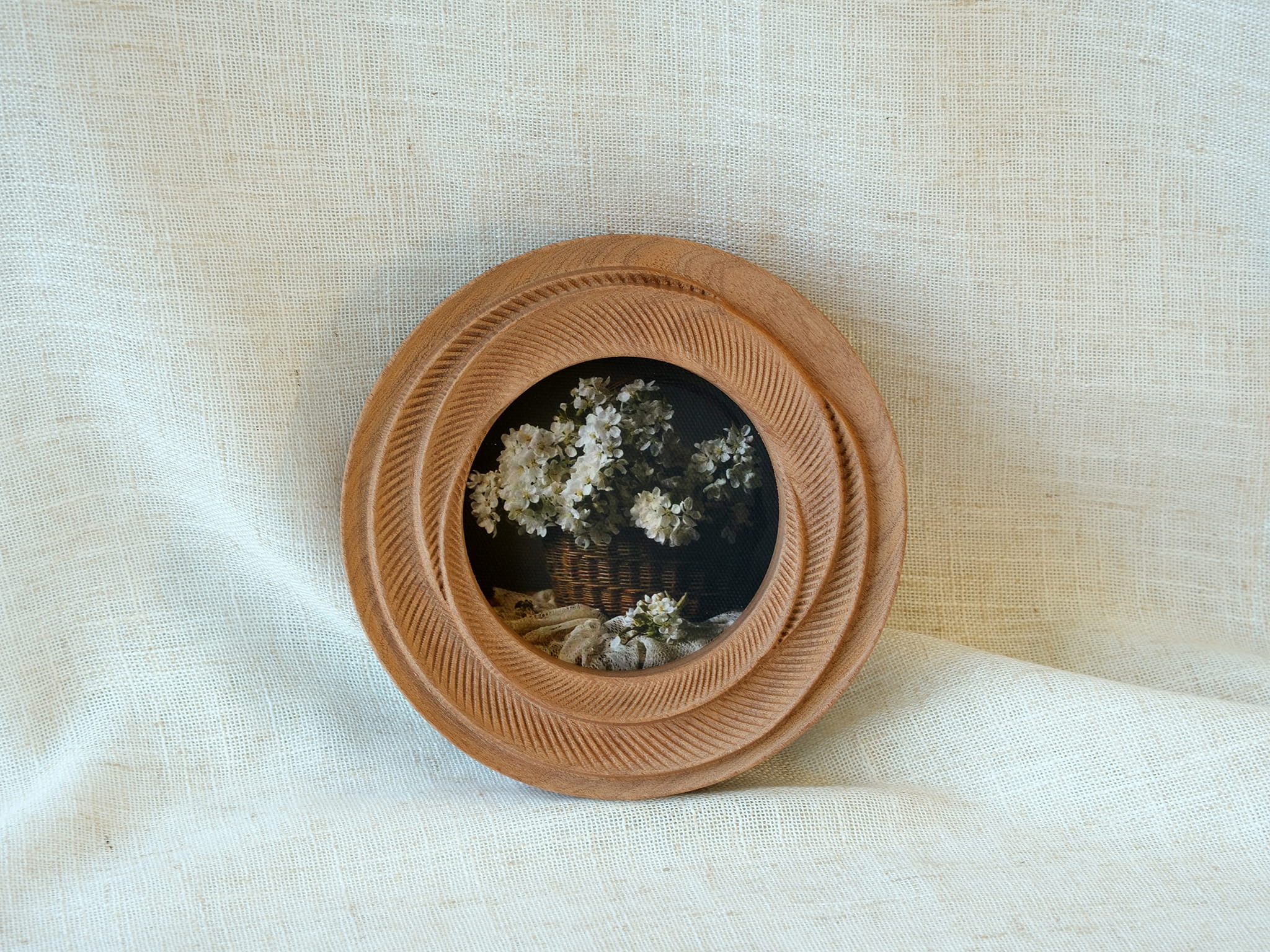 The round flower frame leaning against white fabric, showcasing its radiant tiered textures as artistic desktop decor.