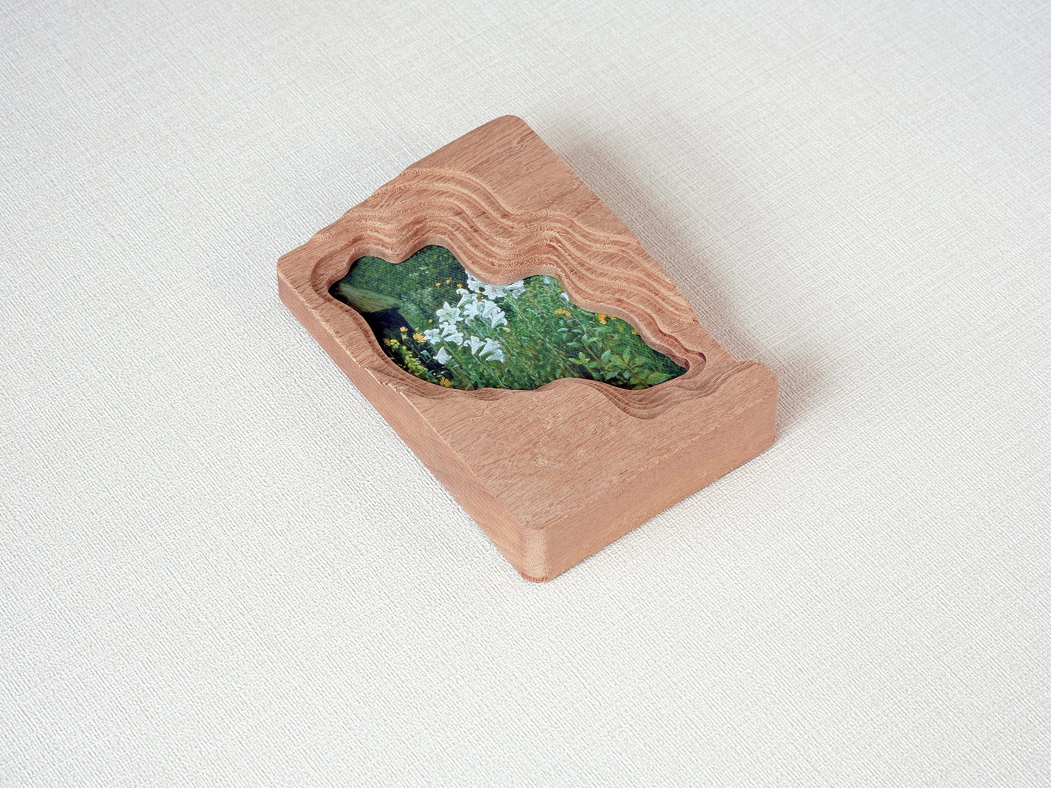 Angled side detail of a handmade solid wood wall art frame with organic lake-shaped cutout and floral meadow artwork.