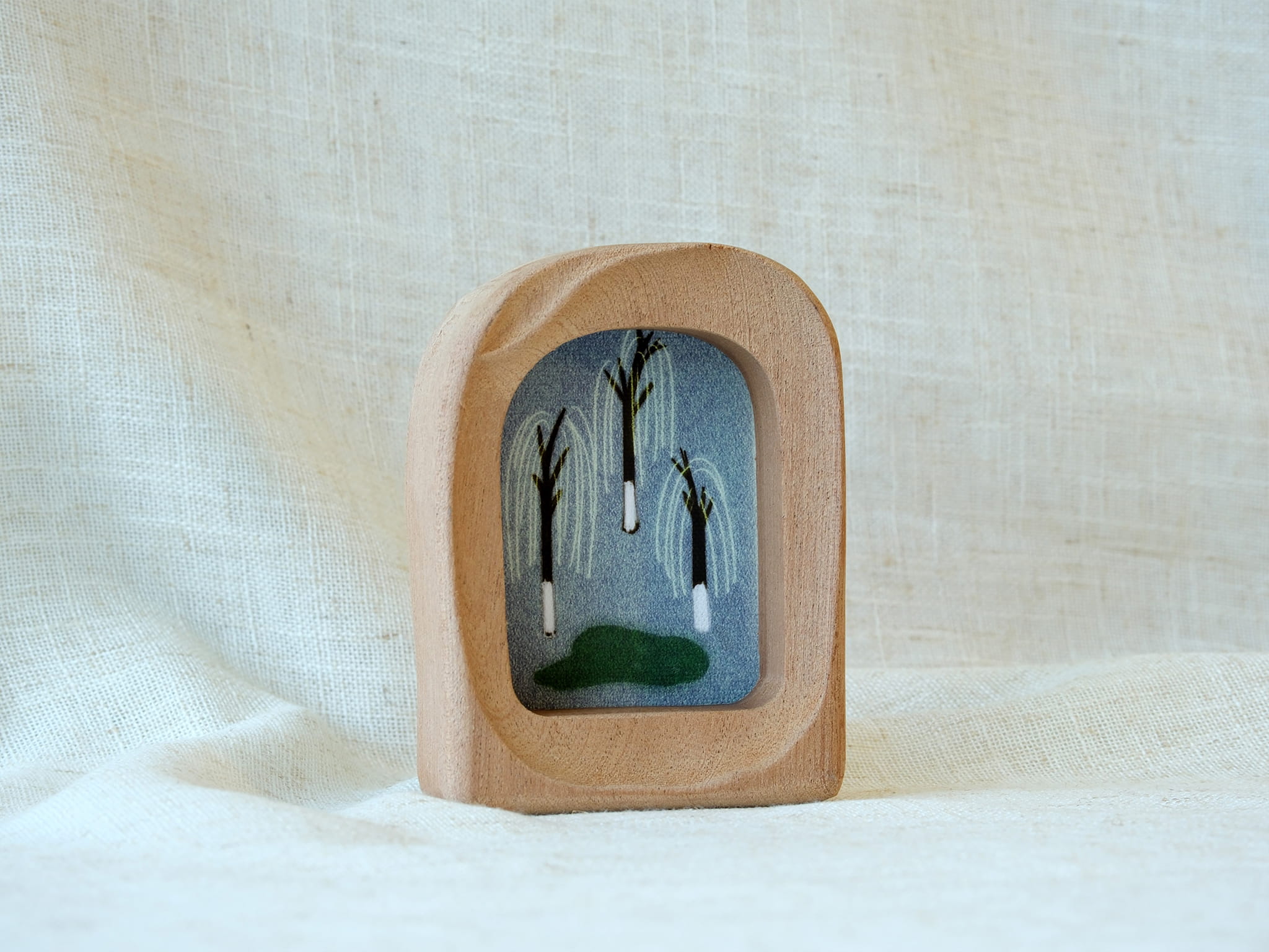 A soft arched wood frame standing firmly on a white textured surface, showcasing its gentle organic silhouette.