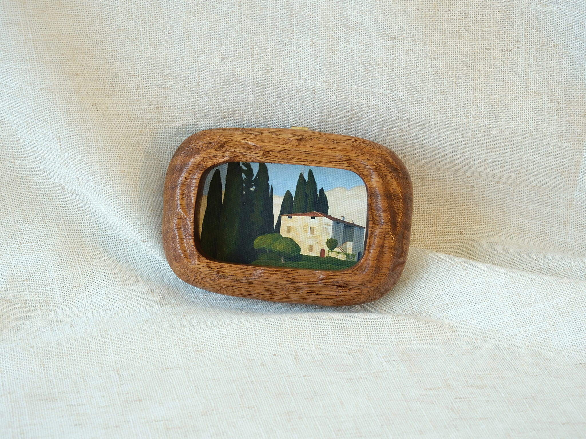 Aesthetic display of a walnut wood art frame on white linen, showing the top metal hanger for wall mounting.