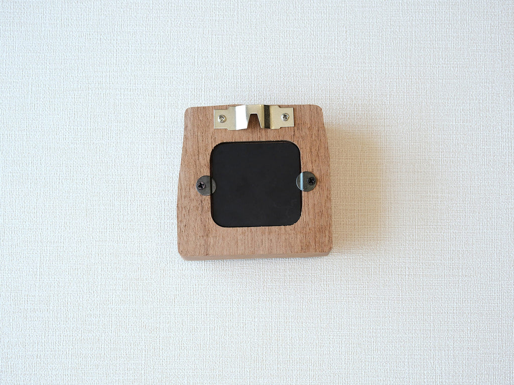 The back view of the mini solid wood frame, showing a silver metal sawtooth hanger for wall mounting and a black backing secured by two turn buttons. The natural grain and clean finish of the Sapele wood are visible on the reverse side.