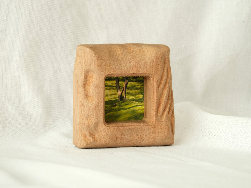 A front-perspective view of the handmade mini square frame standing upright on a white textured surface. The image highlights the frame's stable, thick base and the intricate "Moderno Organico" hand-carved wavy details on the side, creating a sculptural desktop art piece.