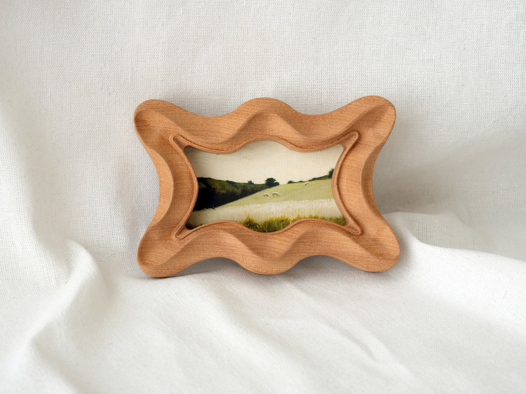 The rippled wave wood frame leaning against a soft white backdrop, highlighting its fluid sculptural silhouette.