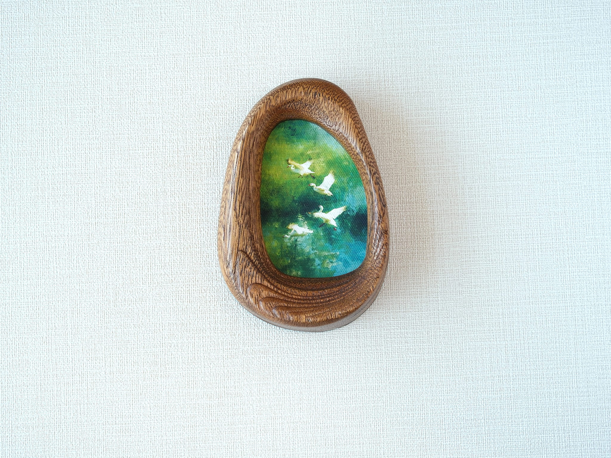 Front view of the Waterdrop handmade solid wood art frame featuring birds flying over a lush forest, highlighting the organic pebble shape and natural wood grain.