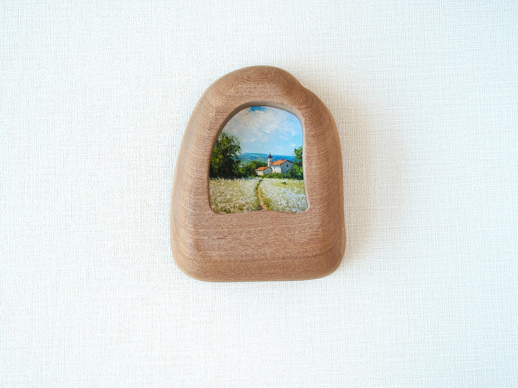 House-shaped wood frame leaning against a soft white textured wall, creating a cozy and natural aesthetic.