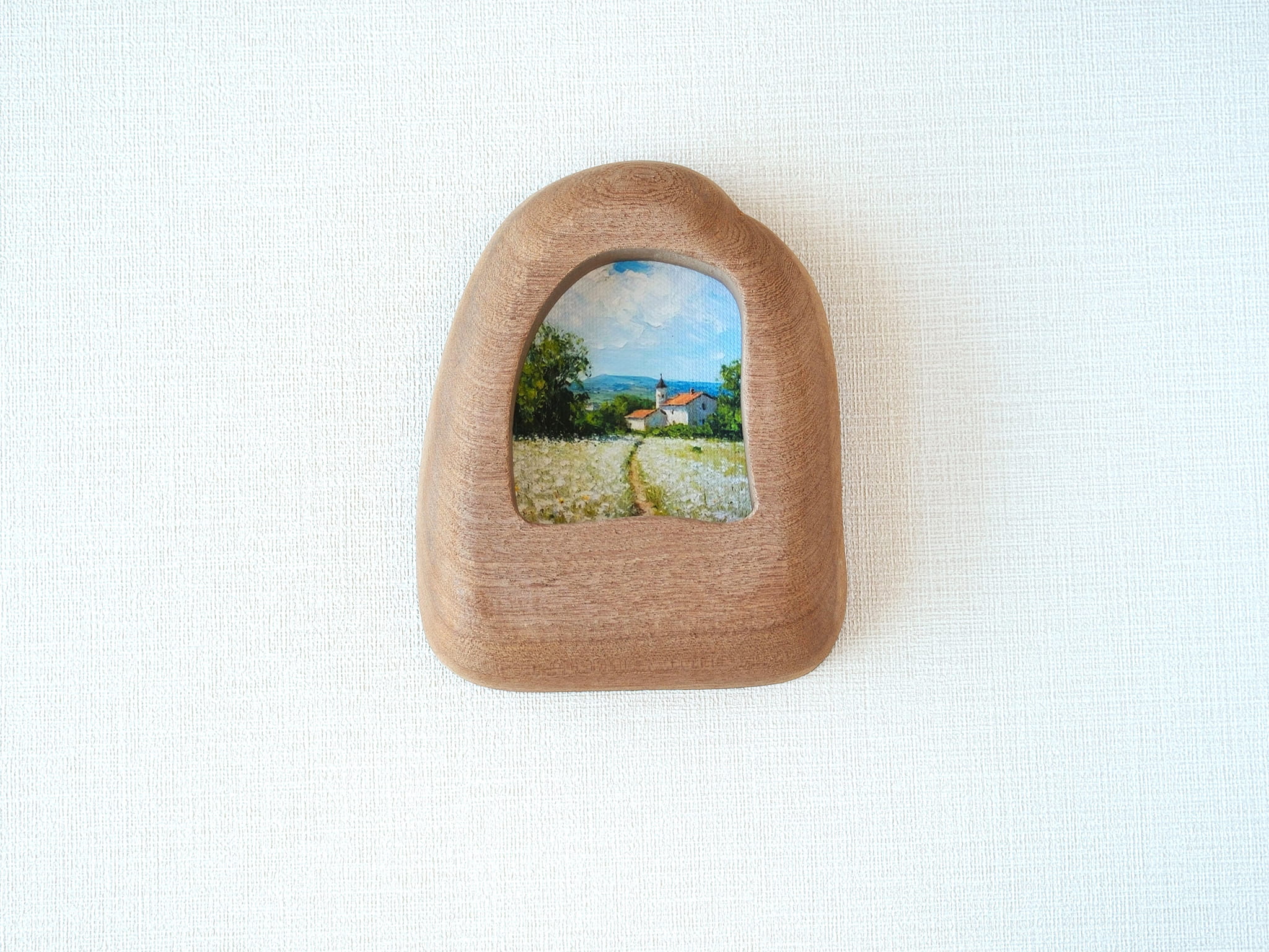 House-shaped wood frame leaning against a soft white textured wall, creating a cozy and natural aesthetic.