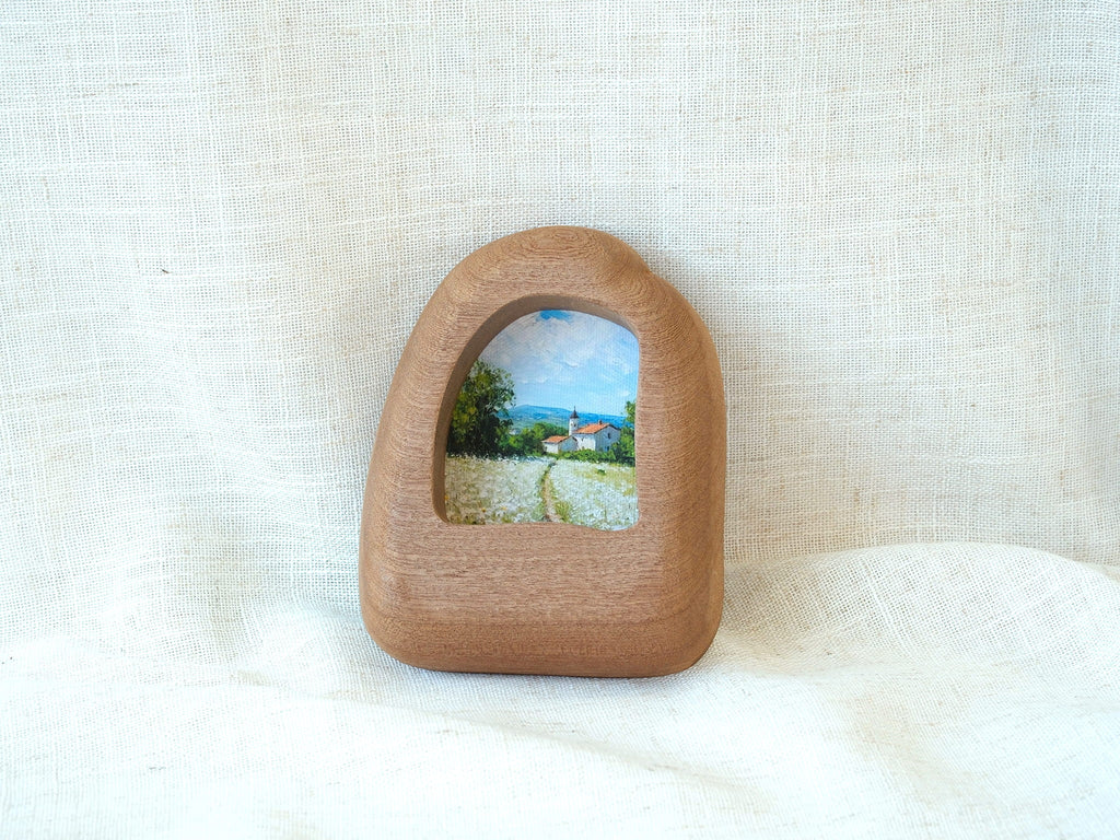 Front view of a house-shaped wood frame, featuring a hand-carved organic silhouette and warm Sapele grain.