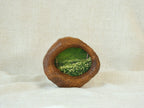 A perspective three-quarter view of the lake-shaped organic solid wood frame standing upright, showcasing the thick handcrafted wood contours and the serene landscape painting of a green meadow filled with wildflowers.