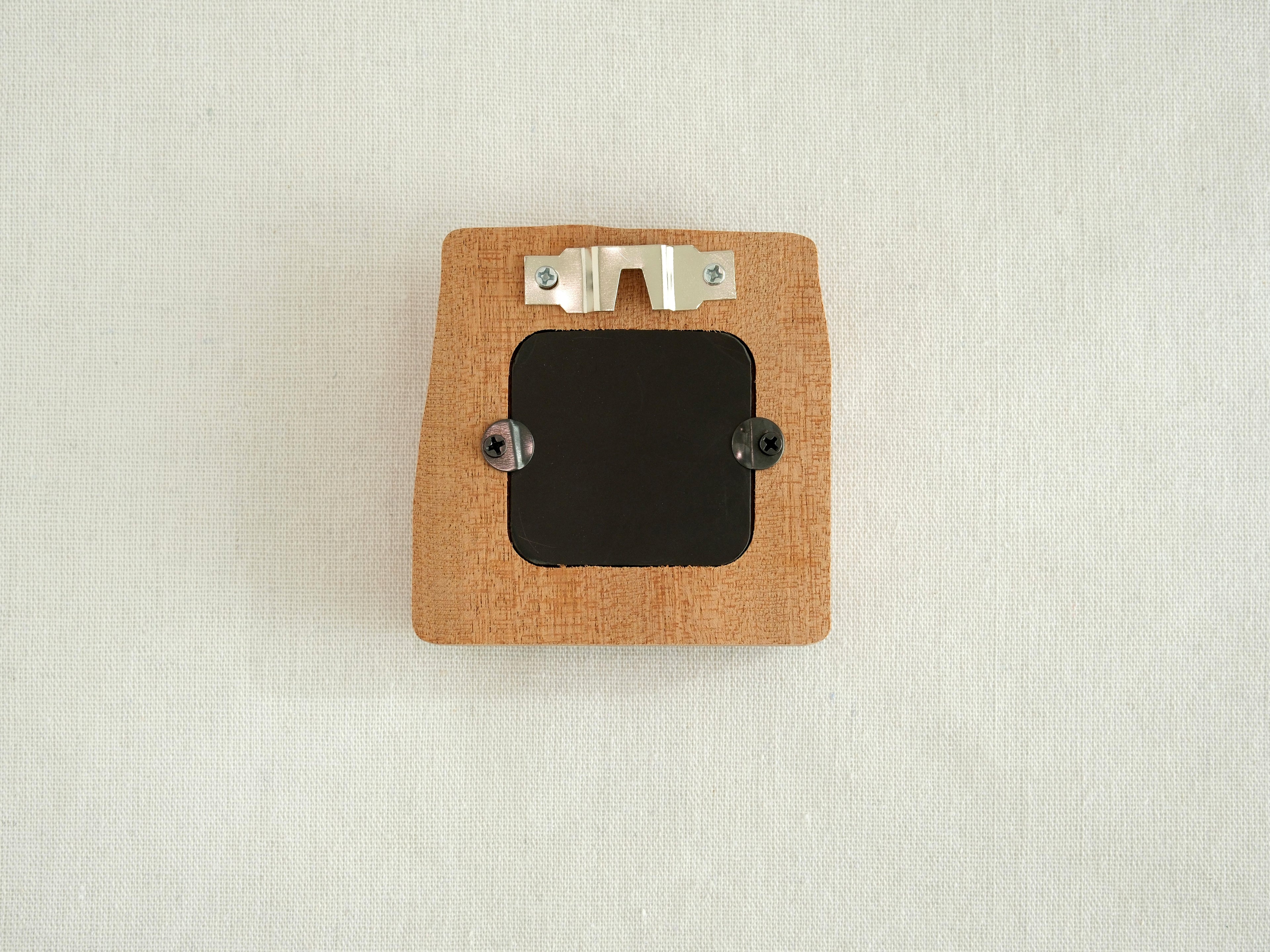 The back view of the mini solid wood frame, showing a silver metal sawtooth hanger for wall mounting and a black backing secured by two turn buttons. The natural grain and clean finish of the Sapele wood are visible on the reverse side.