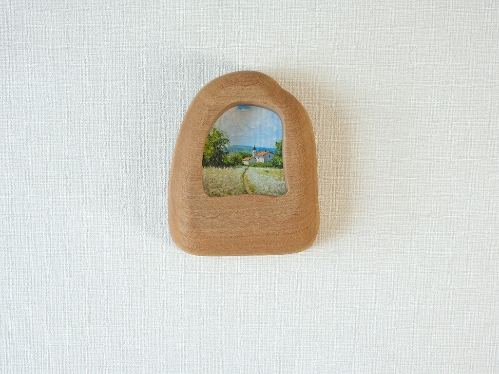 House-shaped wood frame leaning against a soft white textured wall, creating a cozy and natural aesthetic.