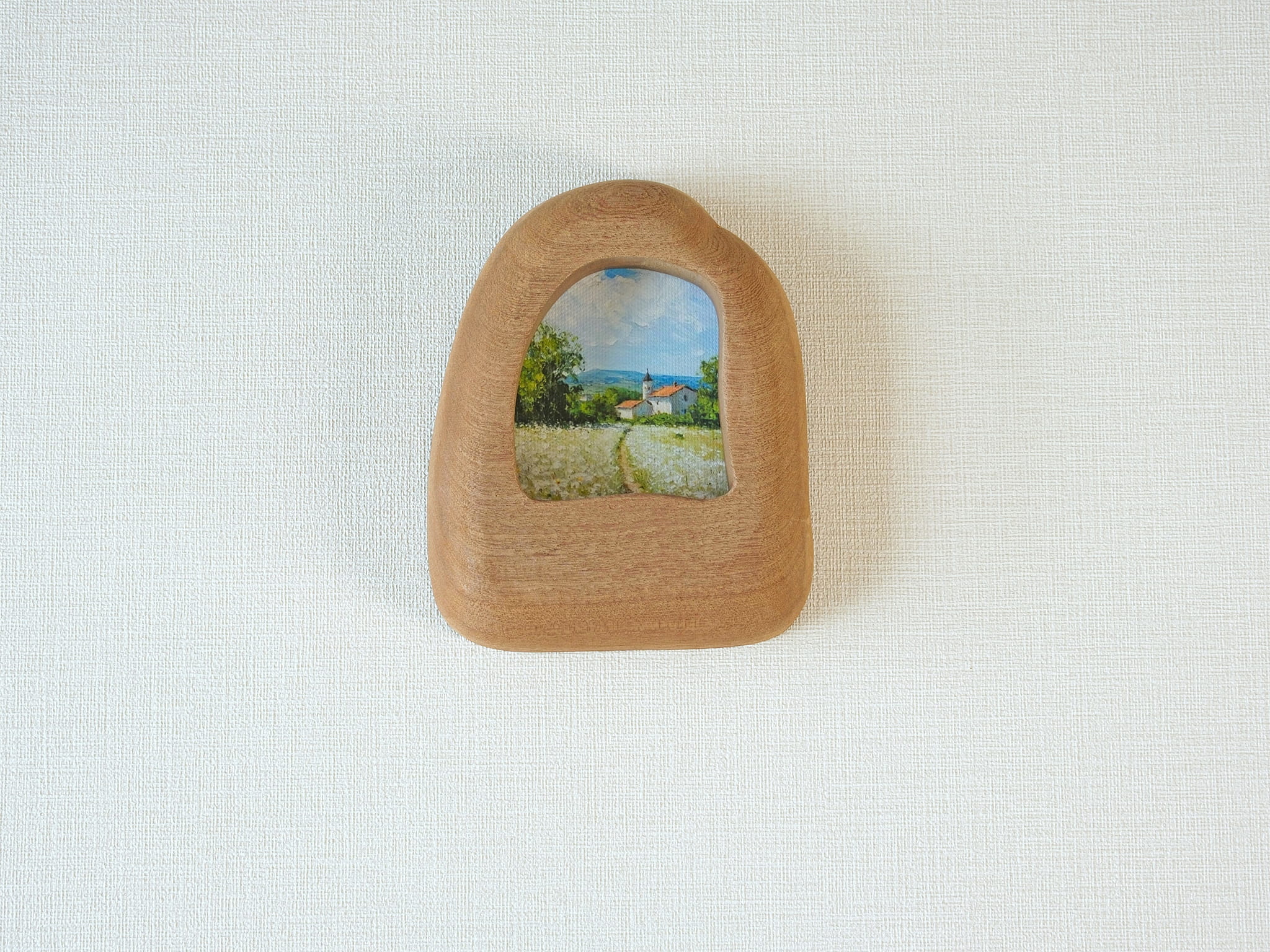 House-shaped wood frame leaning against a soft white textured wall, creating a cozy and natural aesthetic.