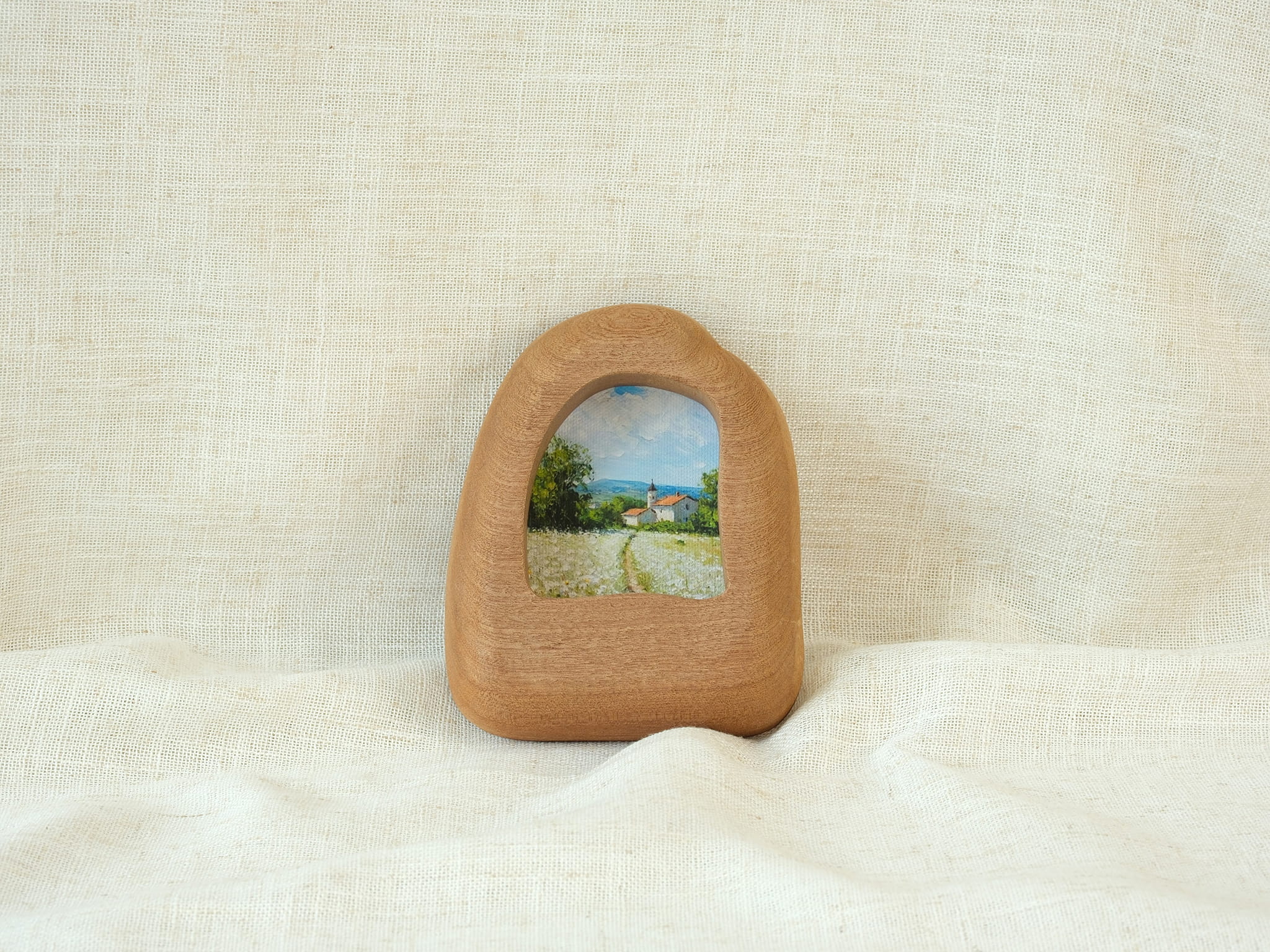 Front view of a house-shaped wood frame, featuring a hand-carved organic silhouette and warm Sapele grain.