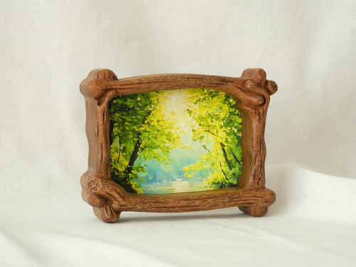 A side-angle view of a handcrafted wood frame with an organic branch-like texture, featuring a vibrant forest sunlight oil painting.