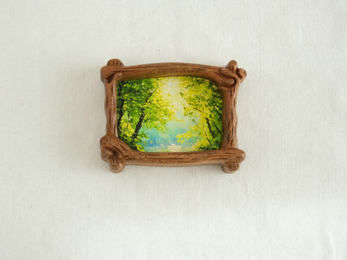 A direct front view of a nature-inspired wood frame with intricate hand-carved bark details, showcasing a lush green forest art piece.