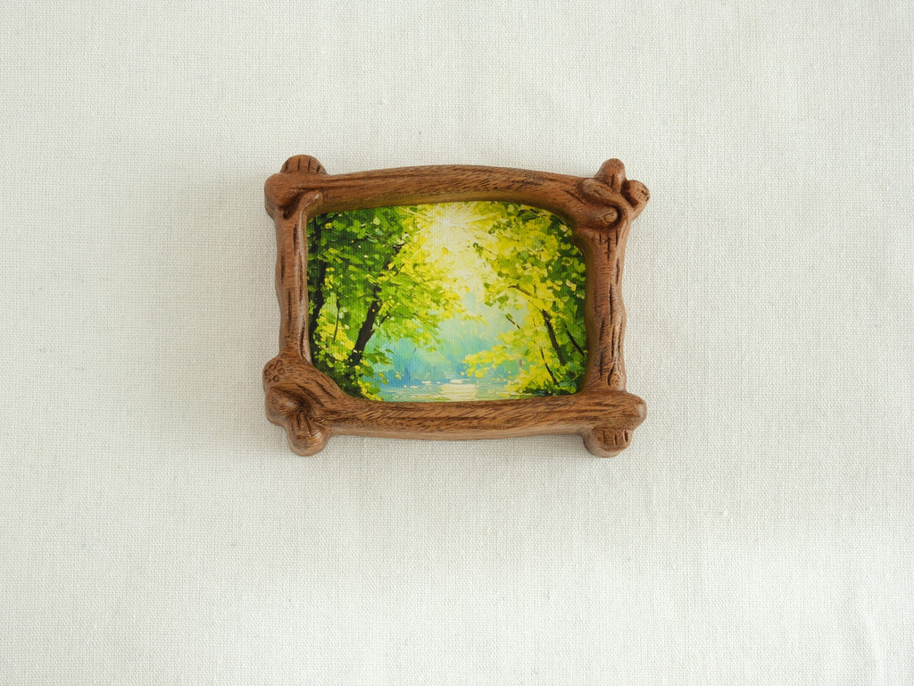 A direct front view of a nature-inspired wood frame with intricate hand-carved bark details, showcasing a lush green forest art piece.