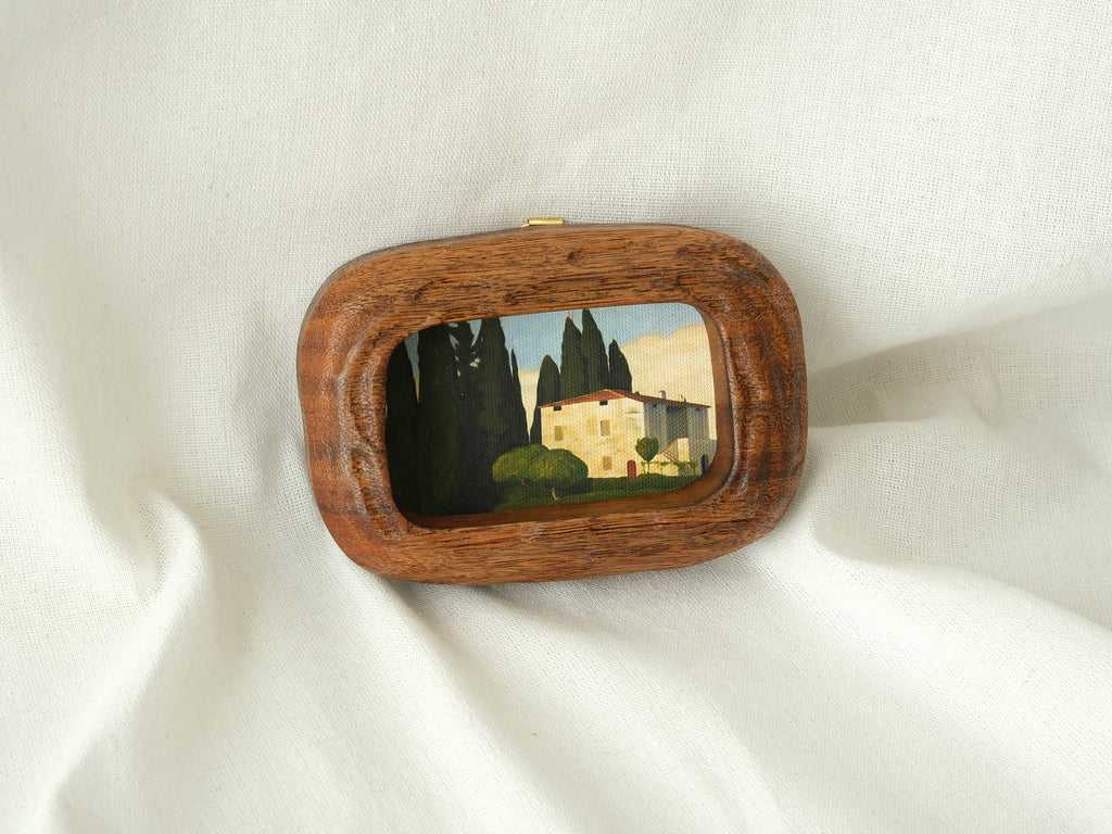 Aesthetic display of a walnut wood art frame on white linen, showing the top metal hanger for wall mounting.